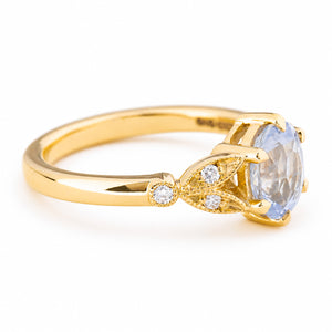 Close up of the side profile of a Vintage-inspired, Blue sapphire and diamond engagement ring in yellow gold.  Showcasing the three accent diamonds.   Set against a clean white background.