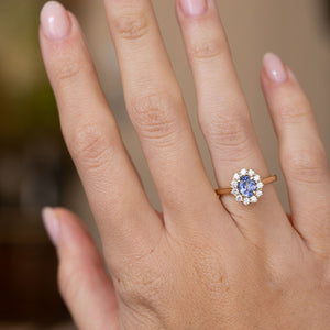Antique-inspired blue sapphire engagement ring worn on the hand, displaying the elegant scale of its oval diamond cluster.