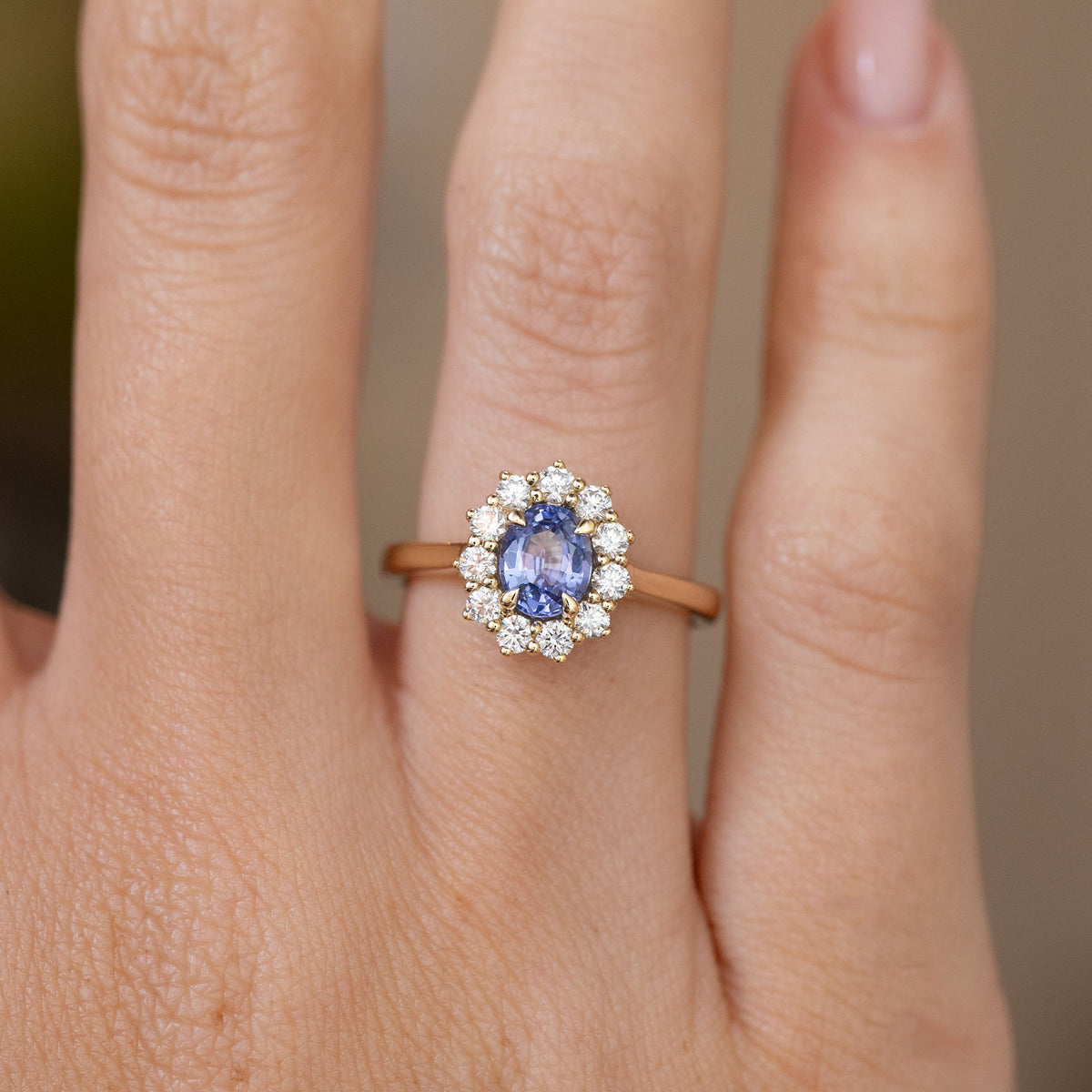Close hand detail of the oval-cut blue sapphire, bright diamond halo and warm yellow gold setting.