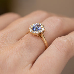 Side-angled view of the blue sapphire engagement ring being worn, revealing its raised cluster setting and slender gold shank.