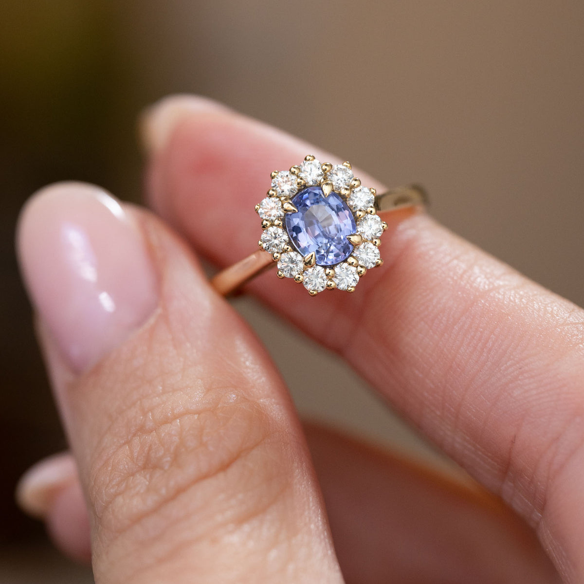 Handheld close-up of the oval sapphire encircled by sparkling round diamonds in a classic yellow gold design.