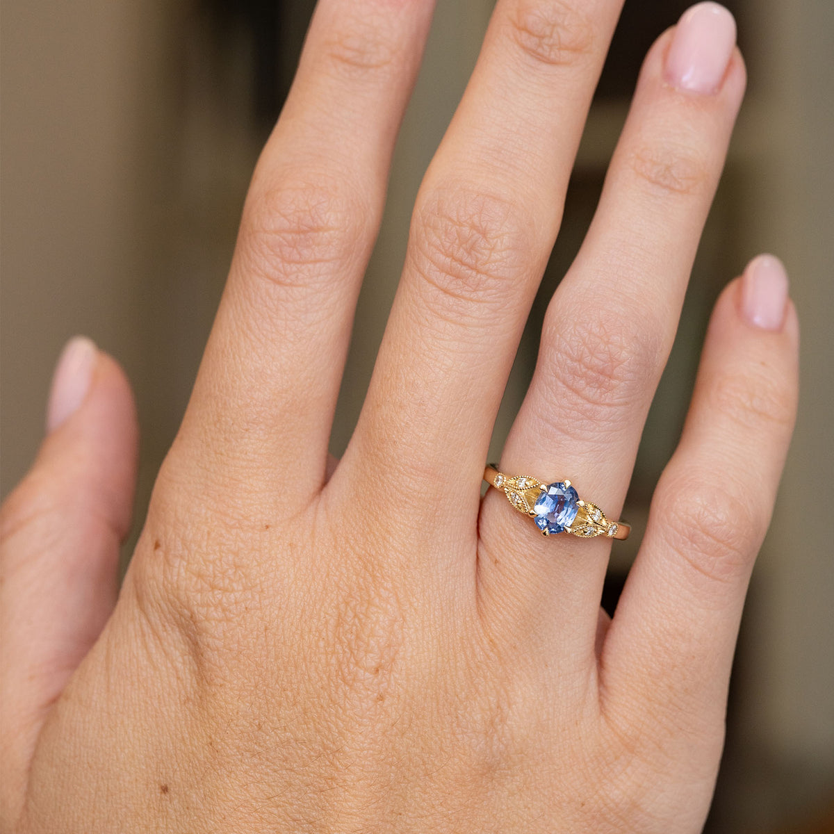 Vintage-inspired blue sapphire engagement ring worn on the hand, showing the elegant proportions of its decorative yellow gold design.