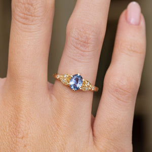 Close-up on the finger highlighting the claw-set sapphire, diamond-accented leaf motifs and fine beaded gold detailing.