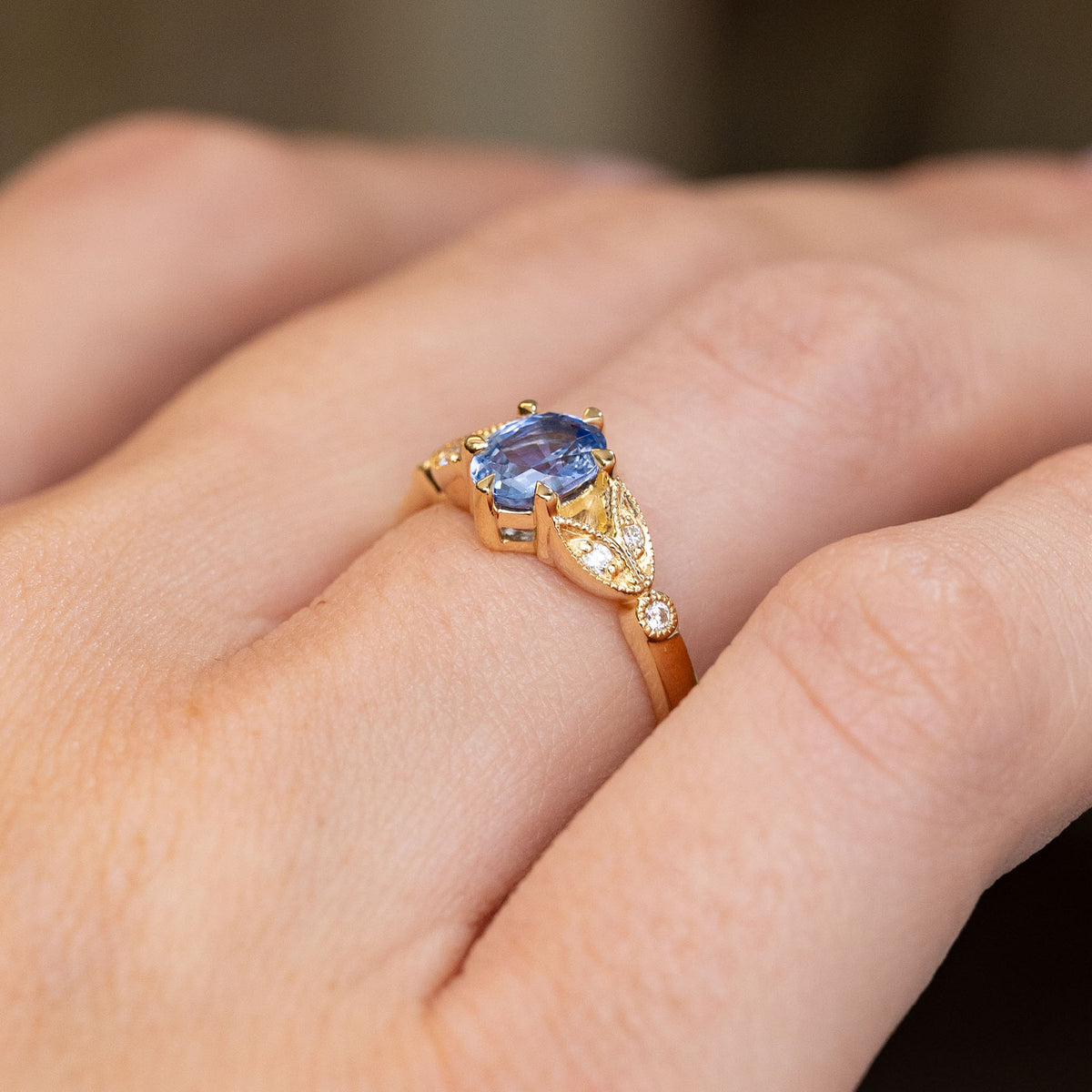 Oblique hand view of the blue sapphire ring, revealing the raised centre setting and intricate diamond-set yellow gold work.