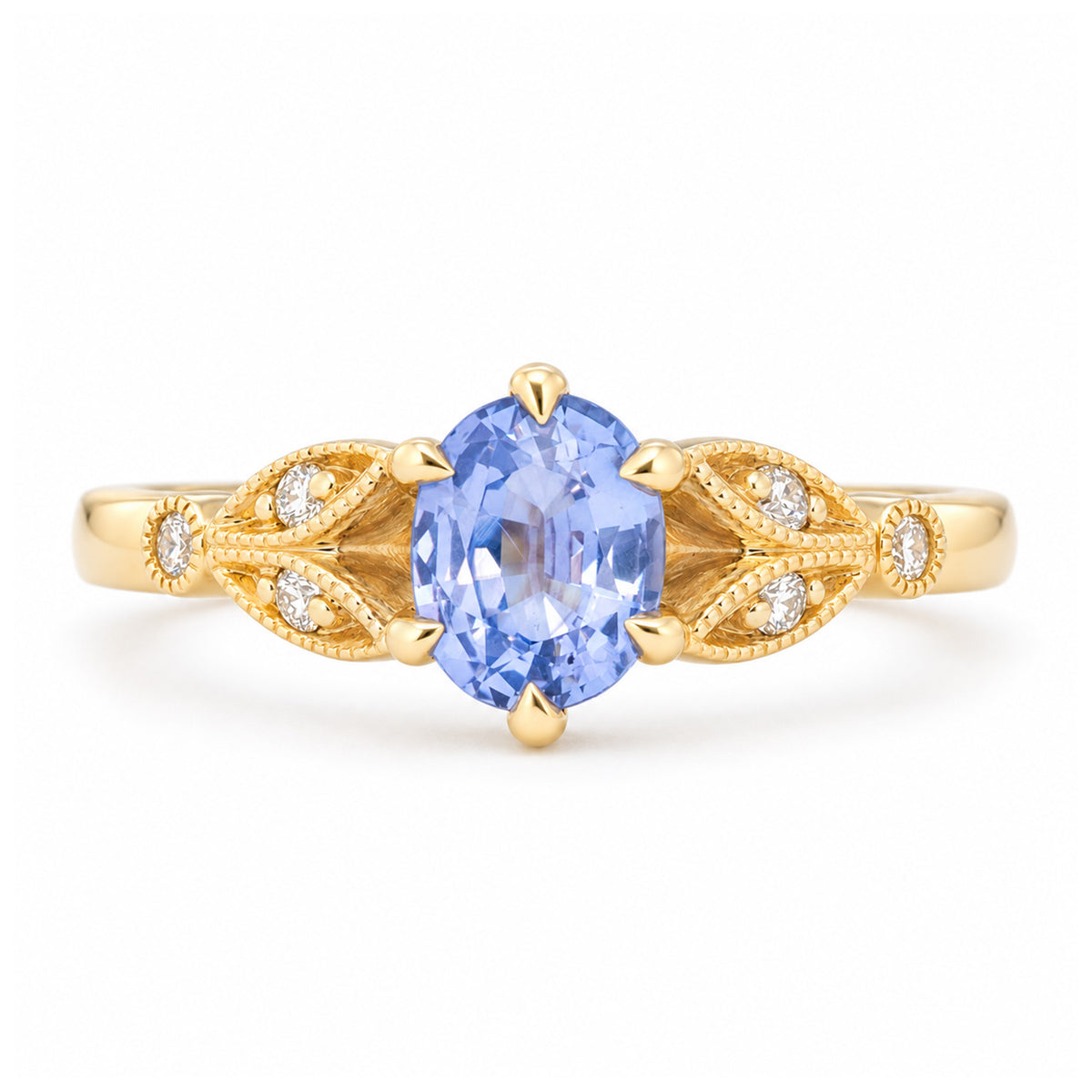 Vintage-inspired oval-cut blue sapphire and diamond engagement ring in yellow gold, featuring ornate leaf-shaped shoulders with diamond accents.