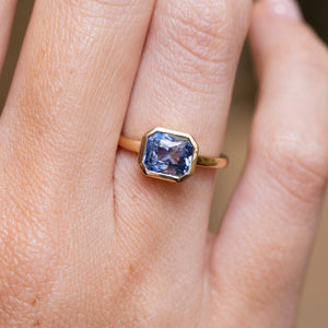 Antique-inspired blue sapphire solitaire engagement ring in yellow gold worn on the finger.