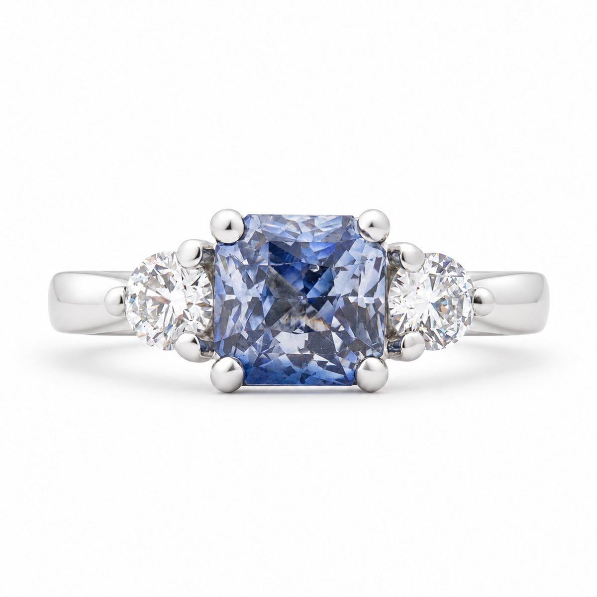Antique-inspired blue sapphire and diamond three-stone engagement ring in platinum, featuring a square cushion-cut sapphire and two round brilliant-cut diamonds.
