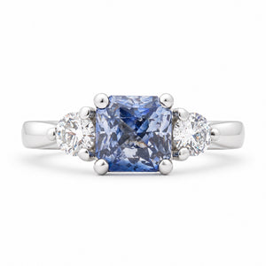 Antique-inspired blue sapphire and diamond three-stone engagement ring in platinum, featuring a square cushion-cut sapphire and two round brilliant-cut diamonds.