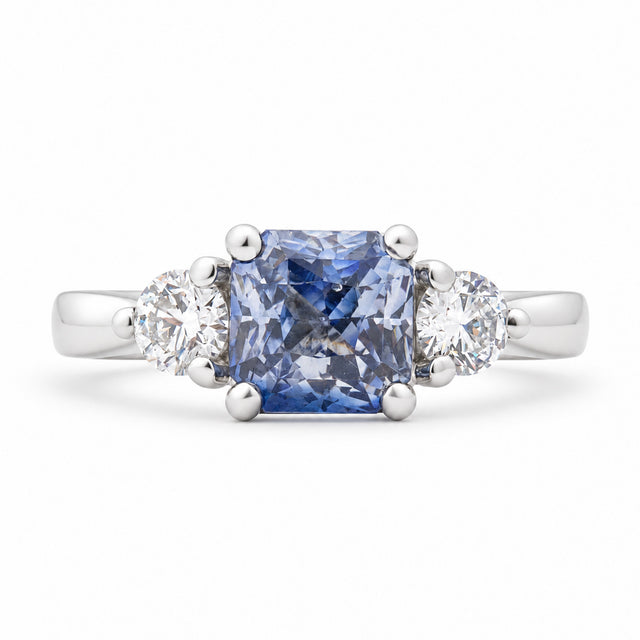 Antique-inspired blue sapphire and diamond three-stone engagement ring in platinum, featuring a square cushion-cut sapphire and two round brilliant-cut diamonds.
