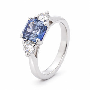 Angled view of the blue sapphire engagement ring, highlighting the raised claw setting and polished platinum band.