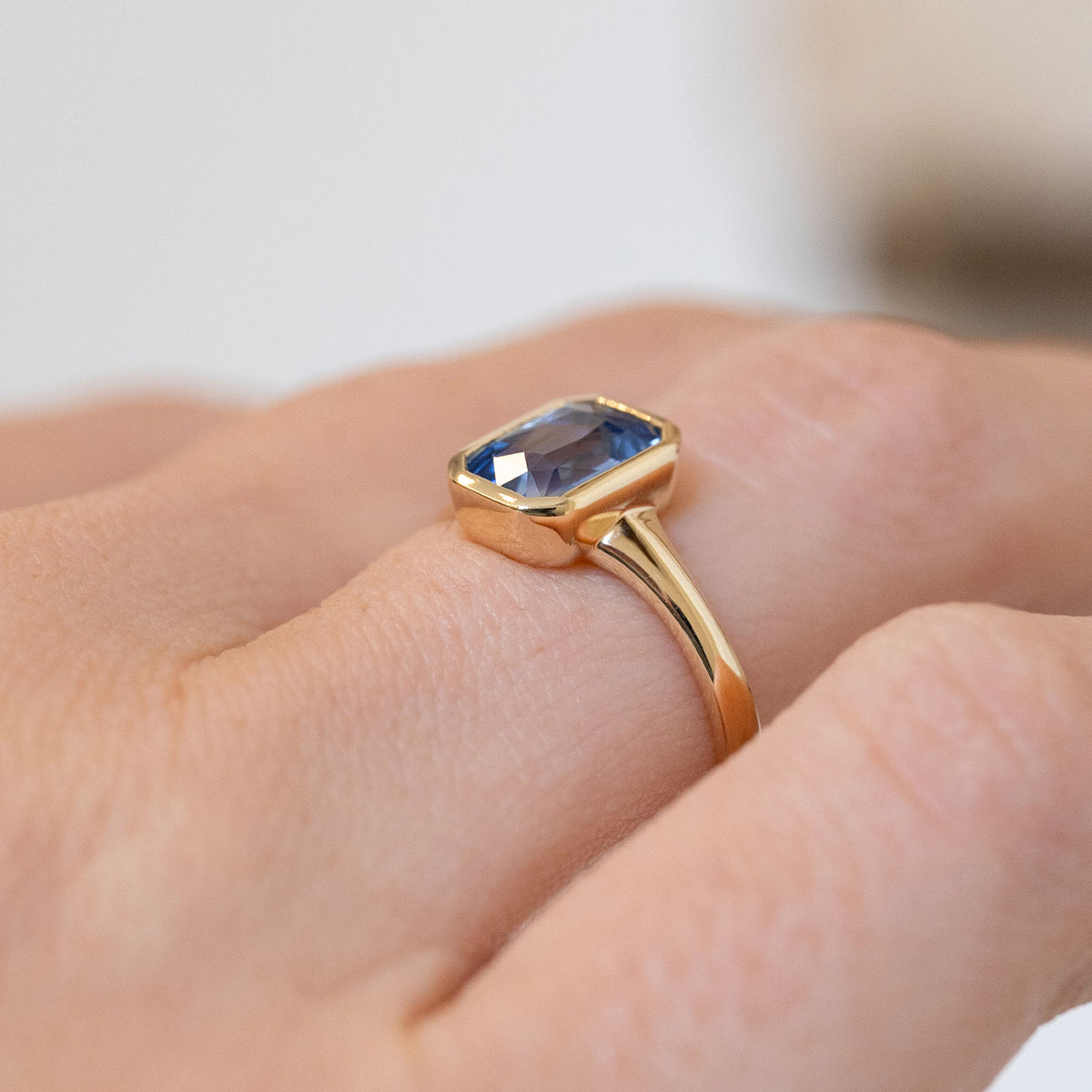 Three-quarter view of the ring being worn, revealing the raised rub-over setting and sculpted yellow gold shoulders.
