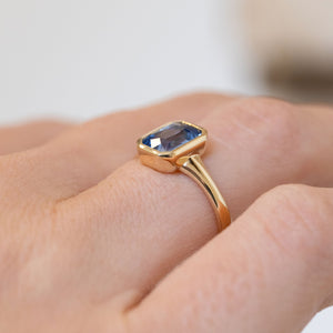 Three-quarter view of the ring being worn, revealing the raised rub-over setting and sculpted yellow gold shoulders.