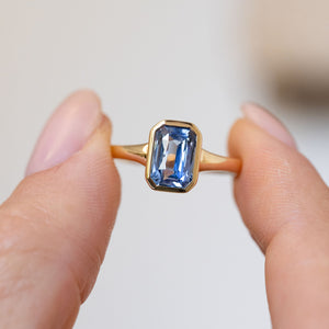 Handheld close-up of the rectangular sky-blue sapphire framed by a sleek polished gold surround.