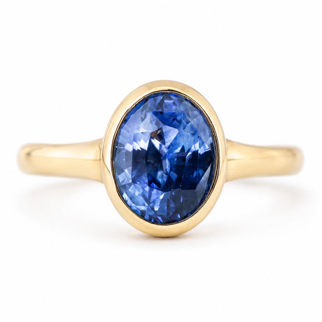 A front profile view of an antique-inspired solitaire ring in yellow gold with a deep blue sapphire at the centre.