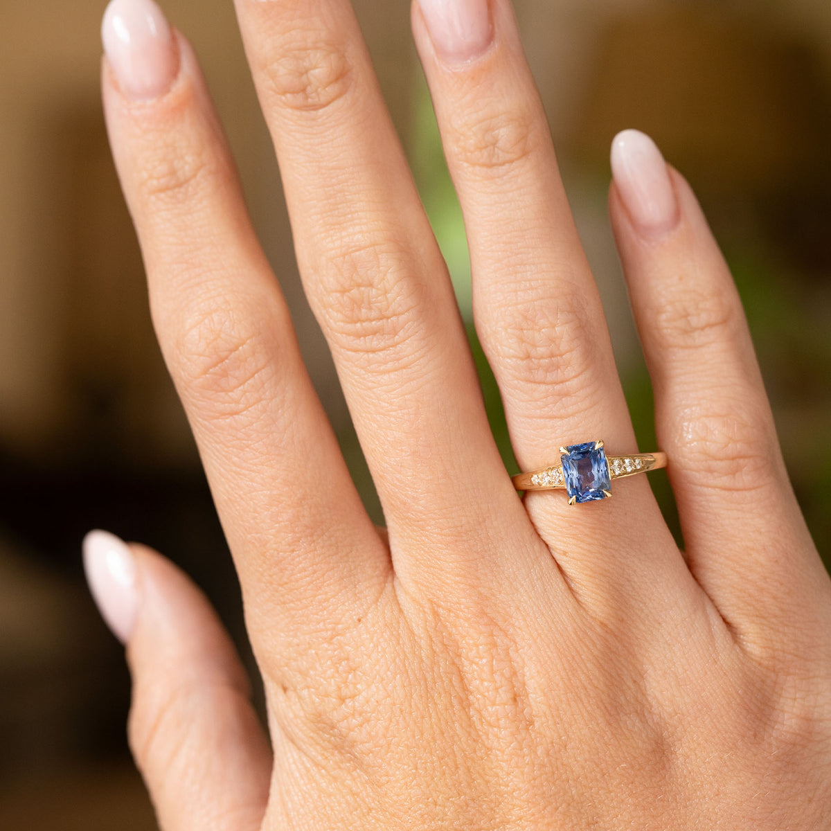 An outstretched hand wearing a Vintage-inspired, Blue sapphire and diamond flanked solitaire engagement ring in yellow gold.