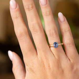 An outstretched hand wearing a Vintage-inspired, Blue sapphire and diamond flanked solitaire engagement ring in yellow gold.