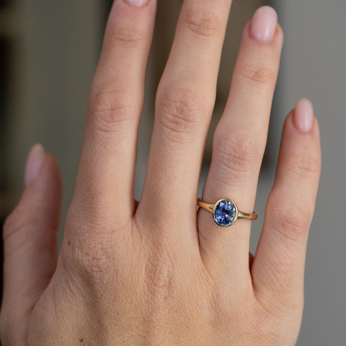 Blue sapphire solitaire displayed on the finger, with rich colour variation framed by a warm yellow gold bezel.