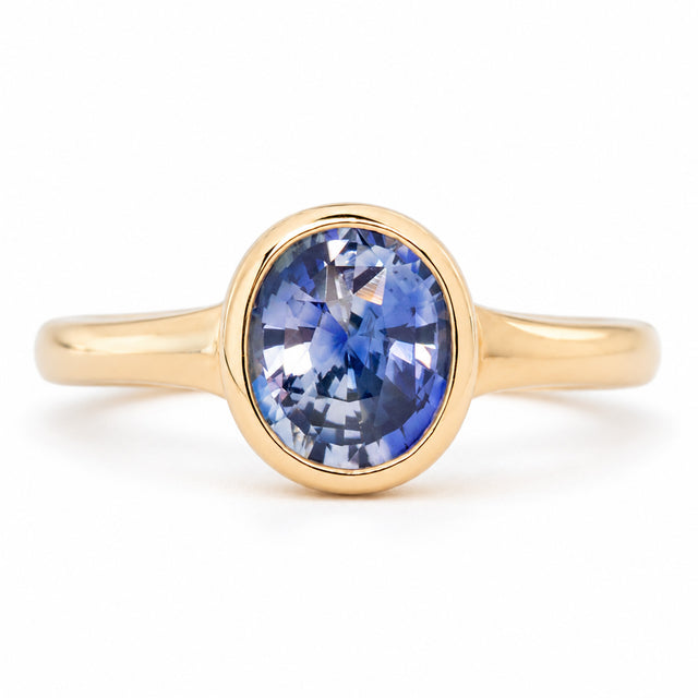 Antique-inspired oval blue sapphire solitaire engagement ring in yellow gold, secured within a sleek rub-over setting.