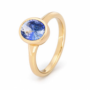 Upright studio view of the sapphire solitaire, highlighting its vibrant oval gemstone, open under-gallery and polished gold band.