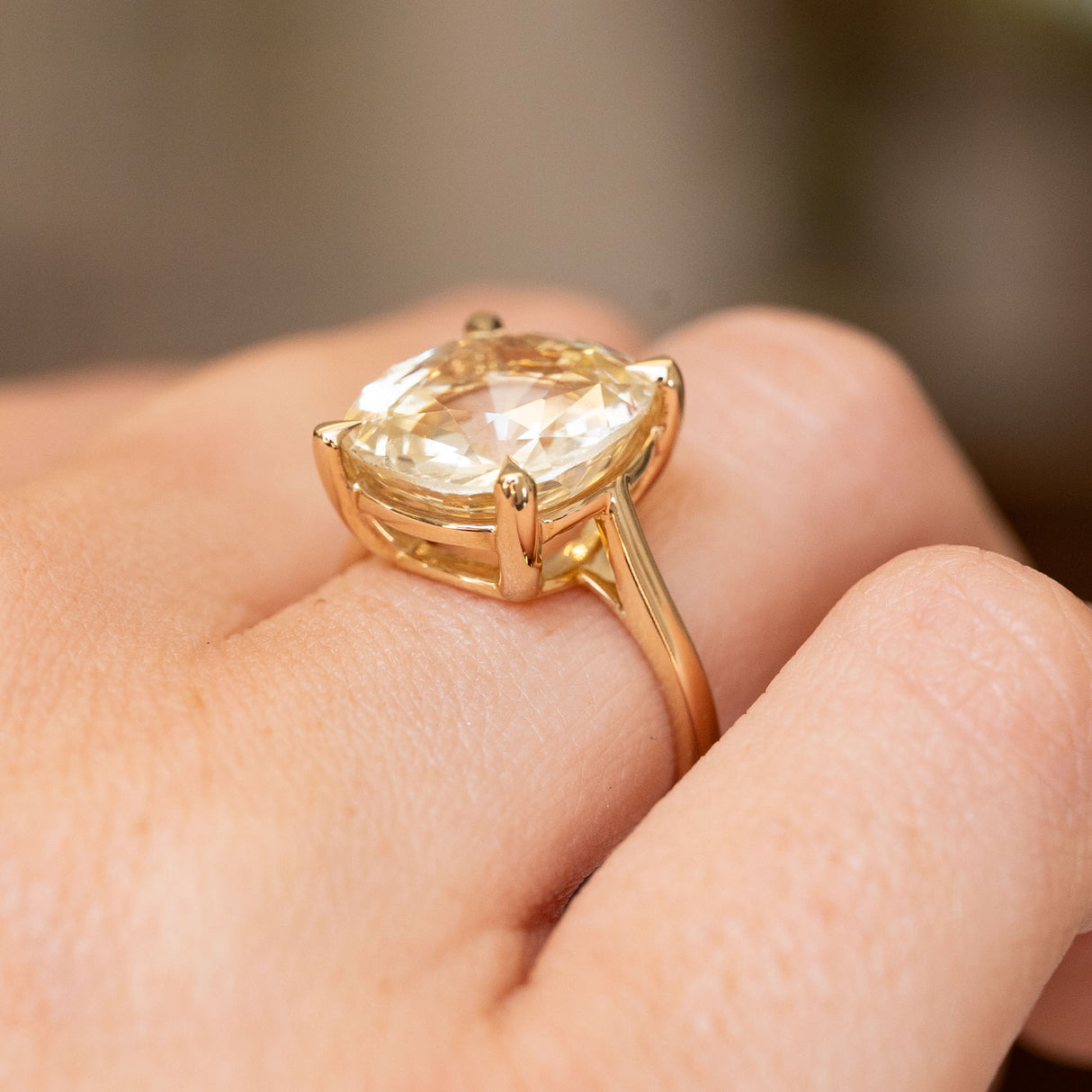 A close-up shot of an Antique-inspired, Yellow sapphire solitaire engagement ring worn on a finger and showed from the side.