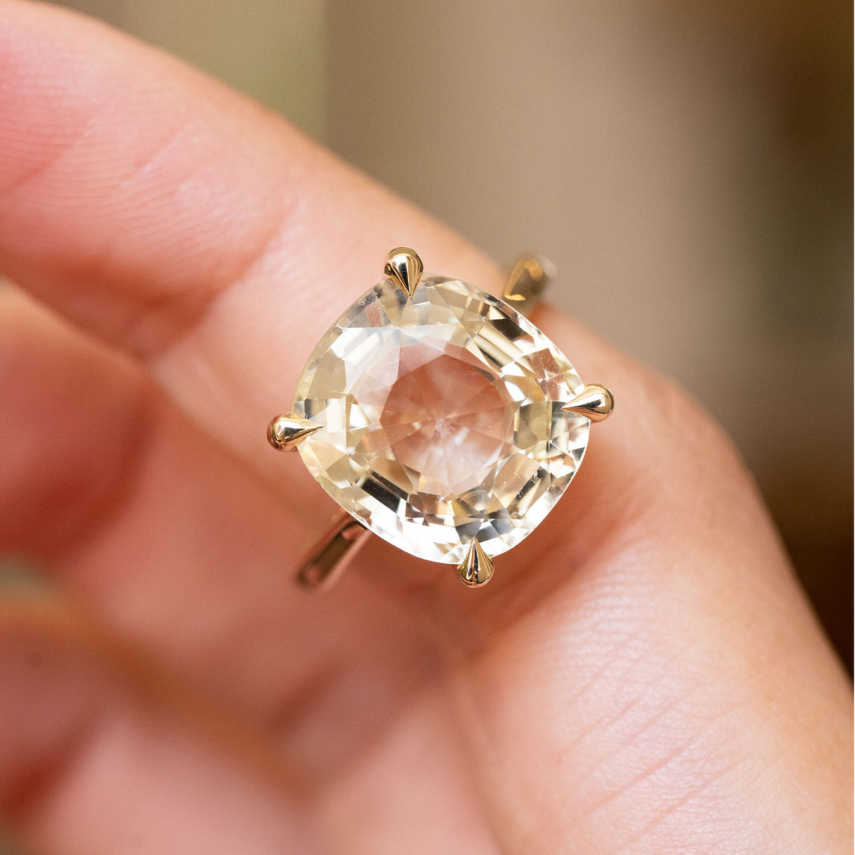 A close-up of a yellow gold Antique-inspired, Yellow sapphire solitaire engagement ring worn on a finger against a blurred background
