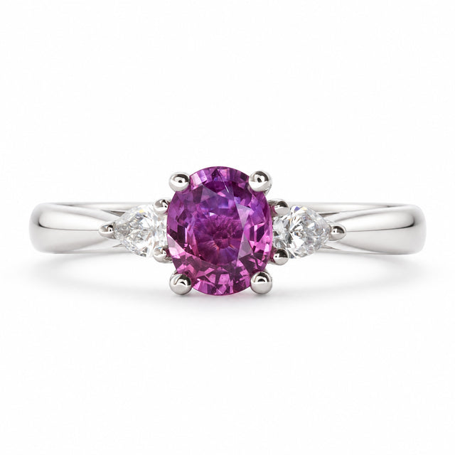 Front view of an antique-inspired three-stone engagement ring with a deep purple-pink sapphire and pear-cut diamonds in platinum.