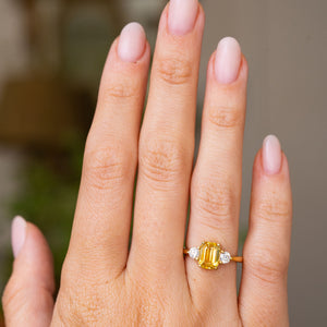 A hand wearing an antique-inspired, Yellow sapphire and diamond three-stone engagement ring in yellow gold shown at a distance