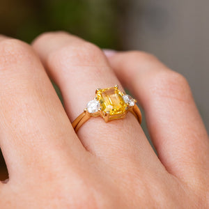 A close-up of a hand wearing a yellow gold Antique-inspired, Yellow sapphire and diamond three-stone engagement ring