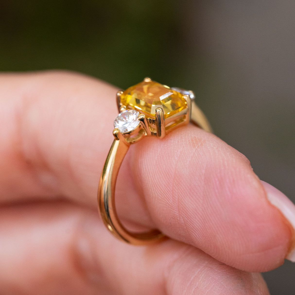 A close-up of a yellow gold Antique-inspired, Yellow sapphire and diamond three-stone engagement ring worn on a finger and shown from the side to display the setting style and height of the ring.