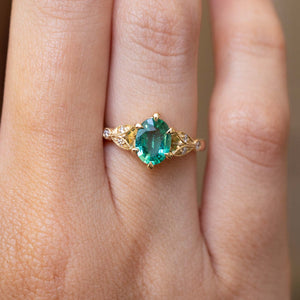 A close-up of a Vintage-inspired, Emerald and diamond engagement ring in yellow gold worn on a finger.
