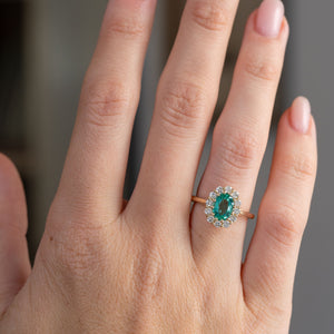 Emerald and diamond engagement ring worn on the hand, showing the elegant proportions of its classic oval cluster design.