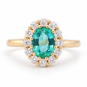 Antique-inspired oval emerald and diamond cluster engagement ring in yellow gold, framed by a halo of round diamonds.