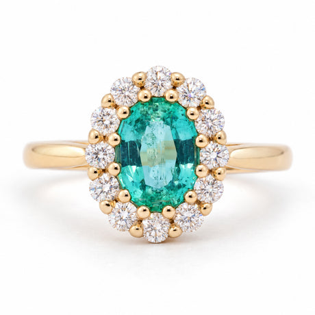 Antique-inspired oval emerald and diamond cluster engagement ring in yellow gold, framed by a halo of round diamonds.