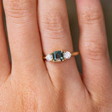 A close-up of a hand wearing a yellow gold Antique-inspired, Teal sapphire and diamond three-stone engagement ring 