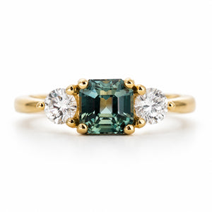 An antique-inspired yellow gold engagement ring set with a green sapphire at the centre, flanked by a diamond on each side.
