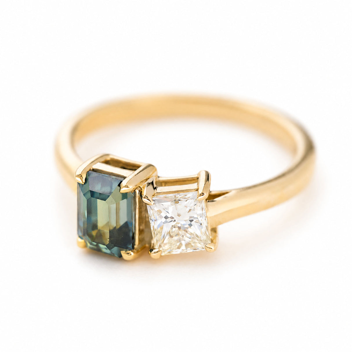 A yellow gold ring featuring a rectangular emerald-cut blue-green sapphire and a princess-cut diamond.