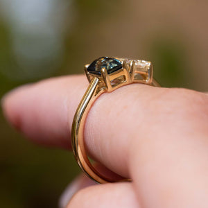 Profile view of Antique-inspired teal sapphire and diamond Toi et Moi engagement ring in yellow gold balanced on the finger.