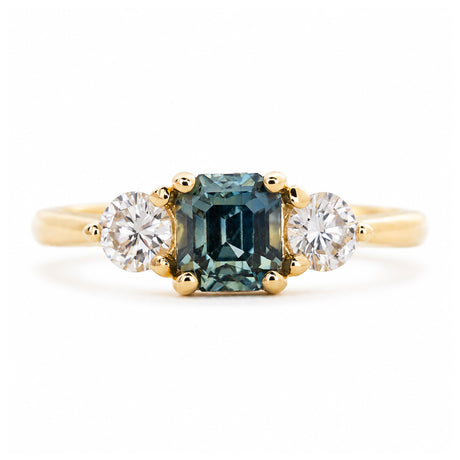 An antique-inspired engagement ring with a teal sapphire at the centre with a round brilliant-cut diamond on each side.