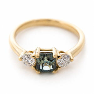 A vintage-inspired yellow gold engagement ring with a teal-green sapphire and diamond three-stone.