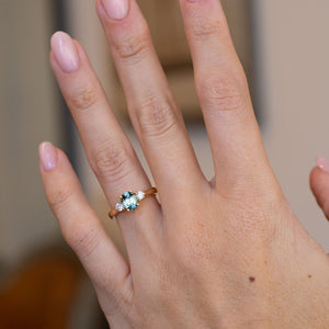 Blue sapphire three-stone engagement ring worn on a hand, showcasing its vibrant blue-green gemstone and elegant proportions.