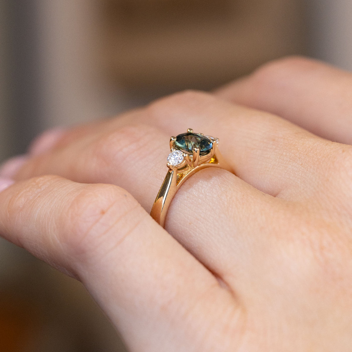 Side-angle view of the teal sapphire ring worn on a hand, highlighting the elevated setting and delicate yellow gold detailing.