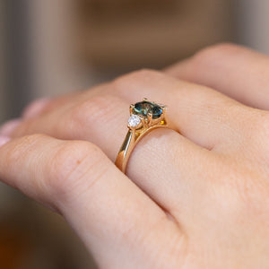 Side-angle view of the teal sapphire ring worn on a hand, highlighting the elevated setting and delicate yellow gold detailing.