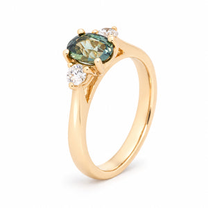 Angled view of the teal sapphire engagement ring, highlighting the raised claw setting and polished yellow gold band.