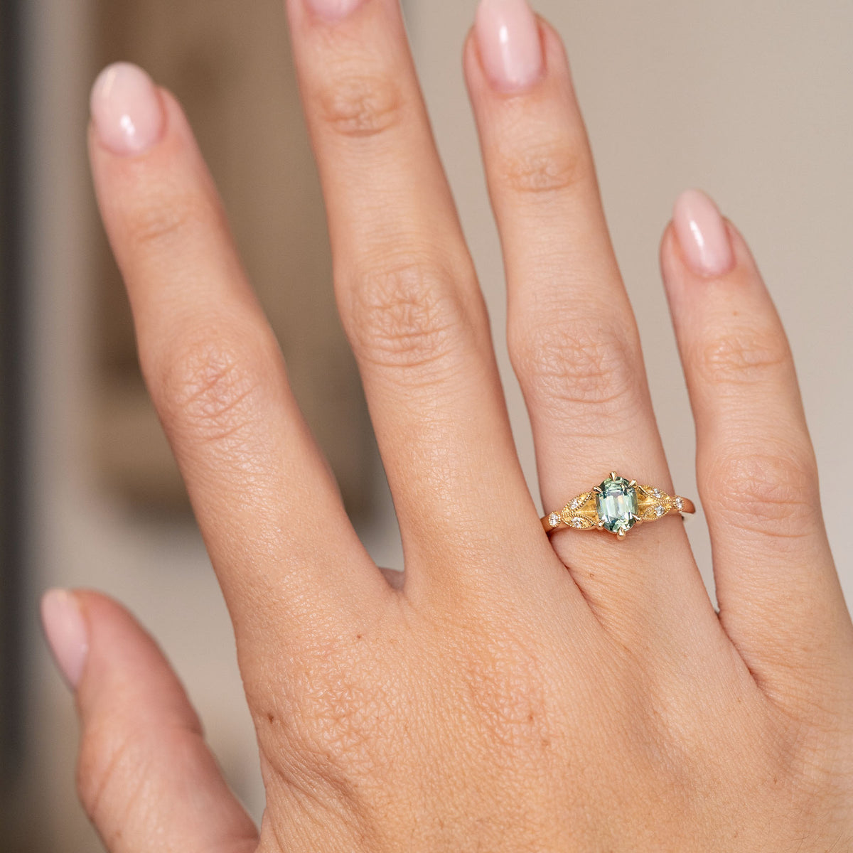Vintage-inspired sapphire and diamond engagement ring worn on the hand, displaying its elegant proportions and soft teal colour.
