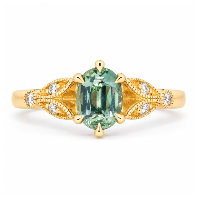 Vintage-inspired teal sapphire and diamond engagement ring in yellow gold, featuring an oval centre stone and ornate diamond-set shoulders.