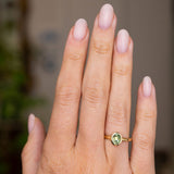 A close-up of a hand wearing a yellow gold Antique-inspired ring on a wedding finger.  An oval green Sri Lankan sapphire is set in the yellow gold band, 