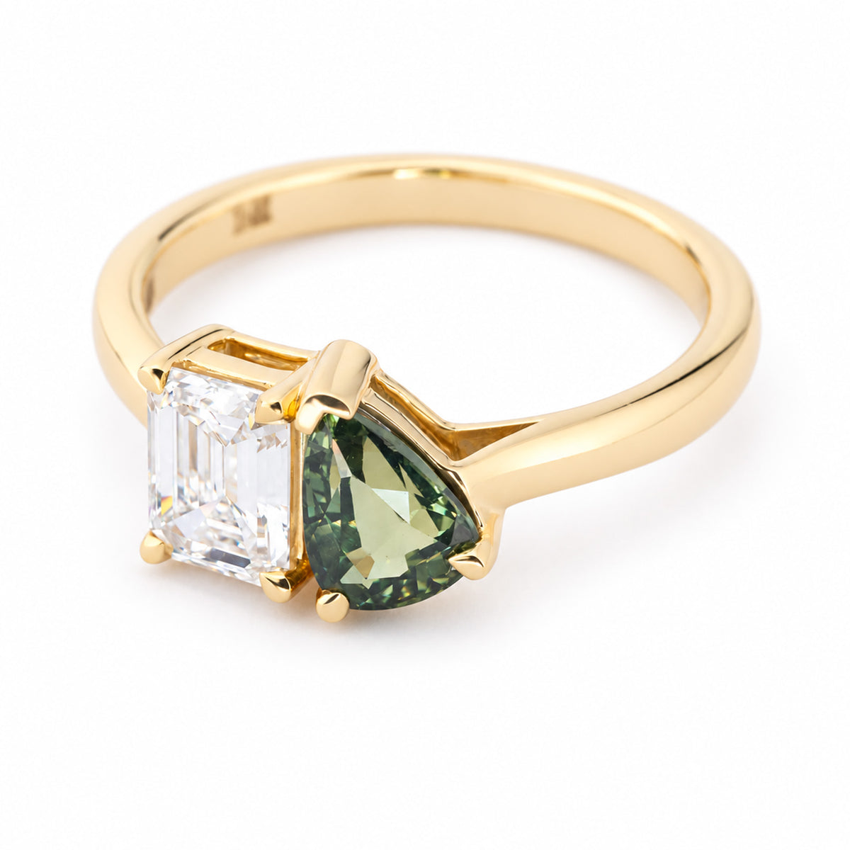 A three-quarter view of a vintage-inspired yellow gold toi et moi engagement ring with a step-cut diamond and green pear-cut sapphire.