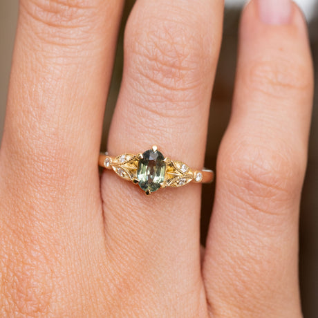 A close-up of a hand wearing a vintage-style Green sapphire and diamond engagement ring