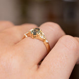 A close-up of a Vintage-inspired, Green sapphire and diamond engagement ring worn on a person's finger.