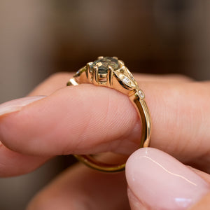 A close-up of a hand wearing a Vintage-inspired, Green sapphire and diamond engagement ring seen from the side to show the gallery.
